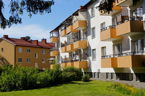 Ett vitt lägenhetshus med gula balkonger. Framför huset är en gräsmatta med buskar. I bakgrunden syns ett gult lägenhetshus.