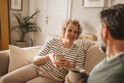 Kvinna sitter i en soffa med båda händerna kring en kaffekopp vänd mot kameran. En man hållandes i en kaffekopp syns med halvt ryggen vänd mot kameran.