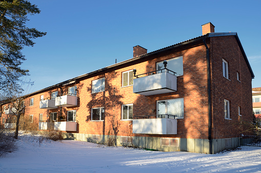 Utsidan av ett lägenhetshus i rött tegel med vita balkonger. Huset har två våningar.